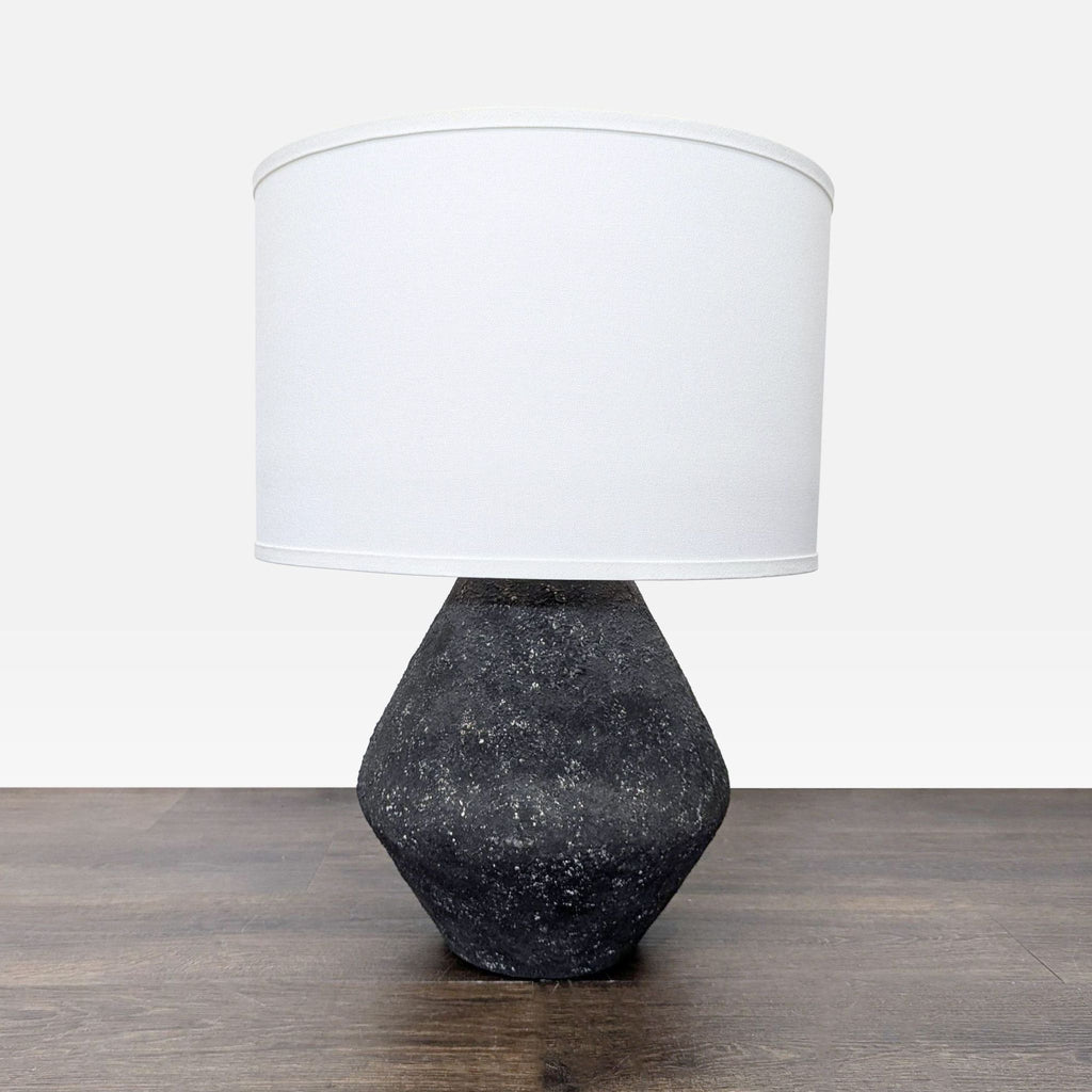 Modern Troy Lighting table lamp with a textured black geometric base and white fabric shade on a wood surface.  