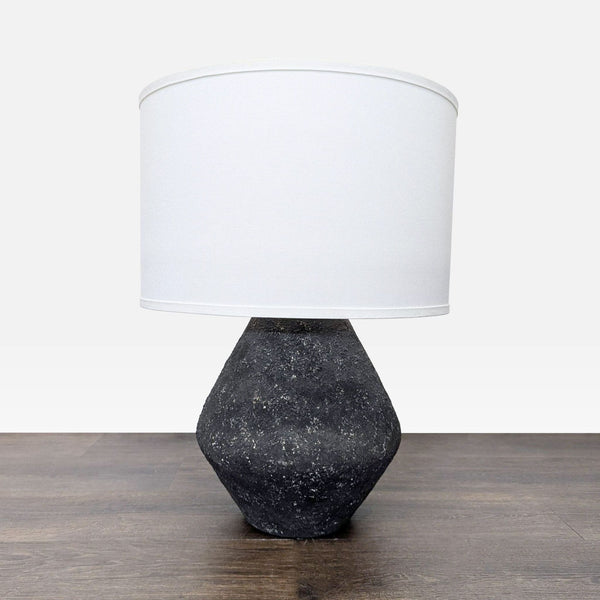 Modern Troy Lighting table lamp with a textured black geometric base and white fabric shade on a wood surface.  
