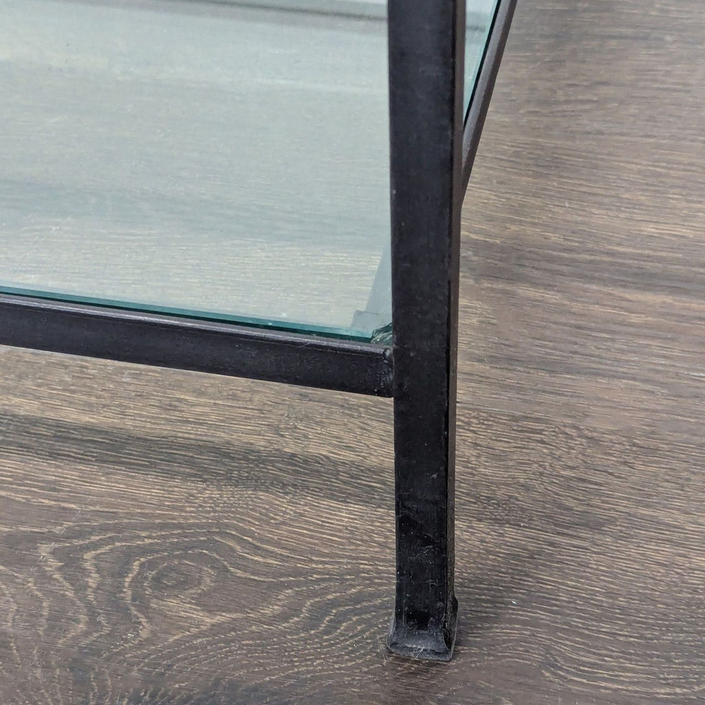 3. Detail of coffee table leg and lower glass shelf with sleek black metal construction.