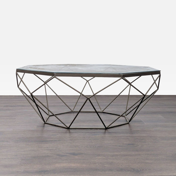 Geometric metal coffee table with a glass top, featuring an angular, modern wireframe base.