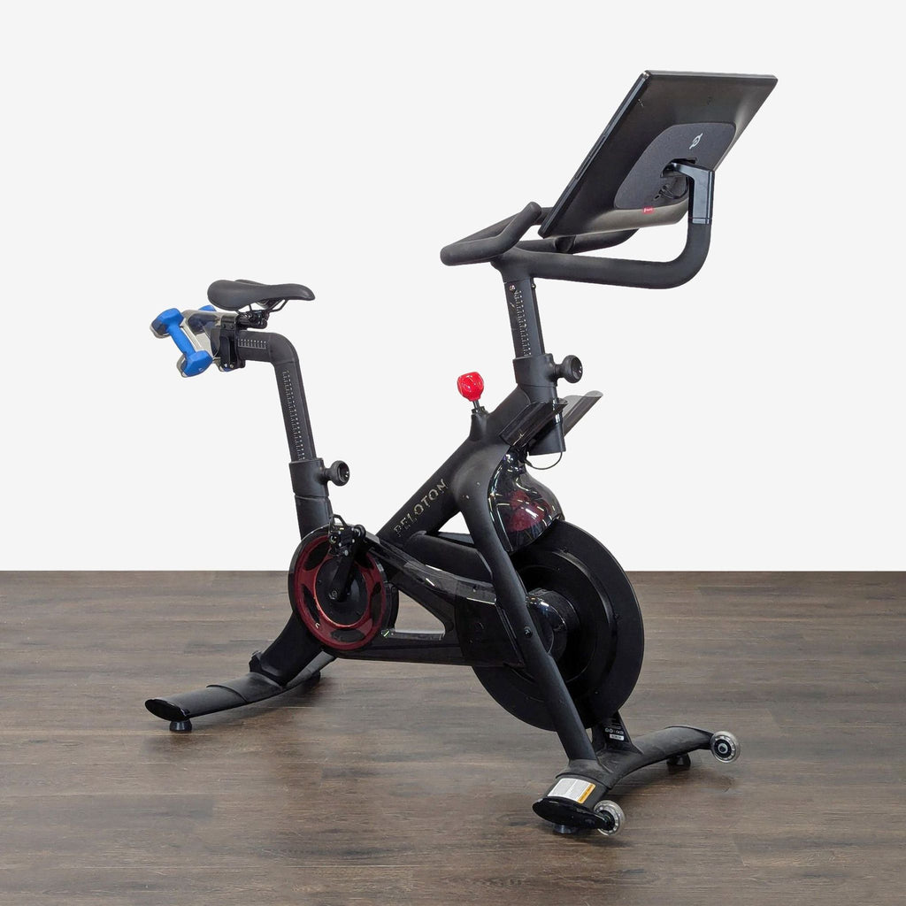 Home gym Peloton bike featuring a large screen, sturdy build, and included blue dumbbells for diverse training.