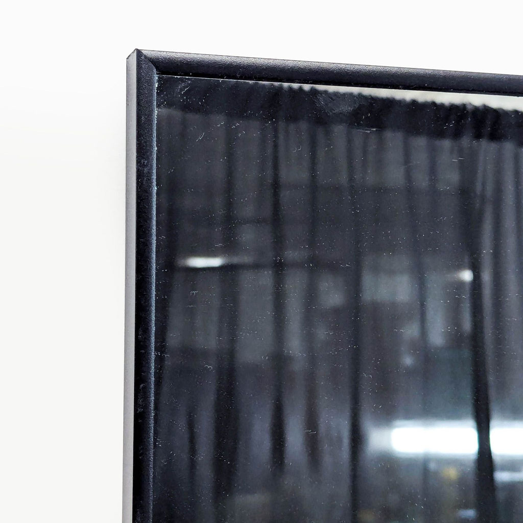 2. Close-up of the upper corner of a black-framed mirror, reflecting a dim indoor scene with curtains.