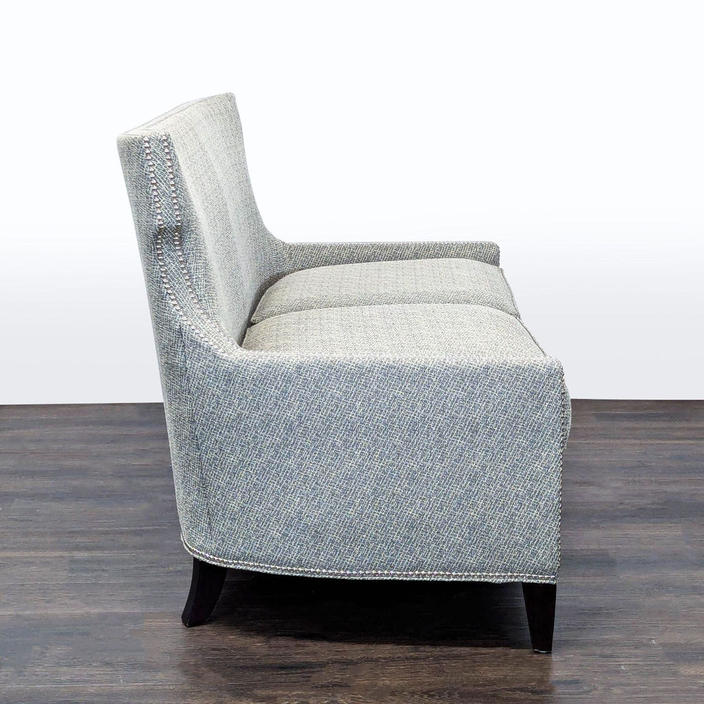 Contemporary Thomasville loveseat in grey upholstery, padded seating, dark wooden legs, and stylish nailhead detail.
