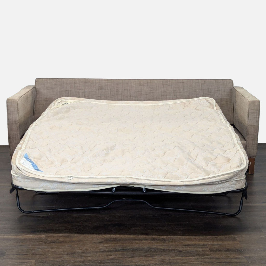 Convertible tan sleeper sofa with soft upholstery, clean lines, and sturdy wood base, fitting various decors.  