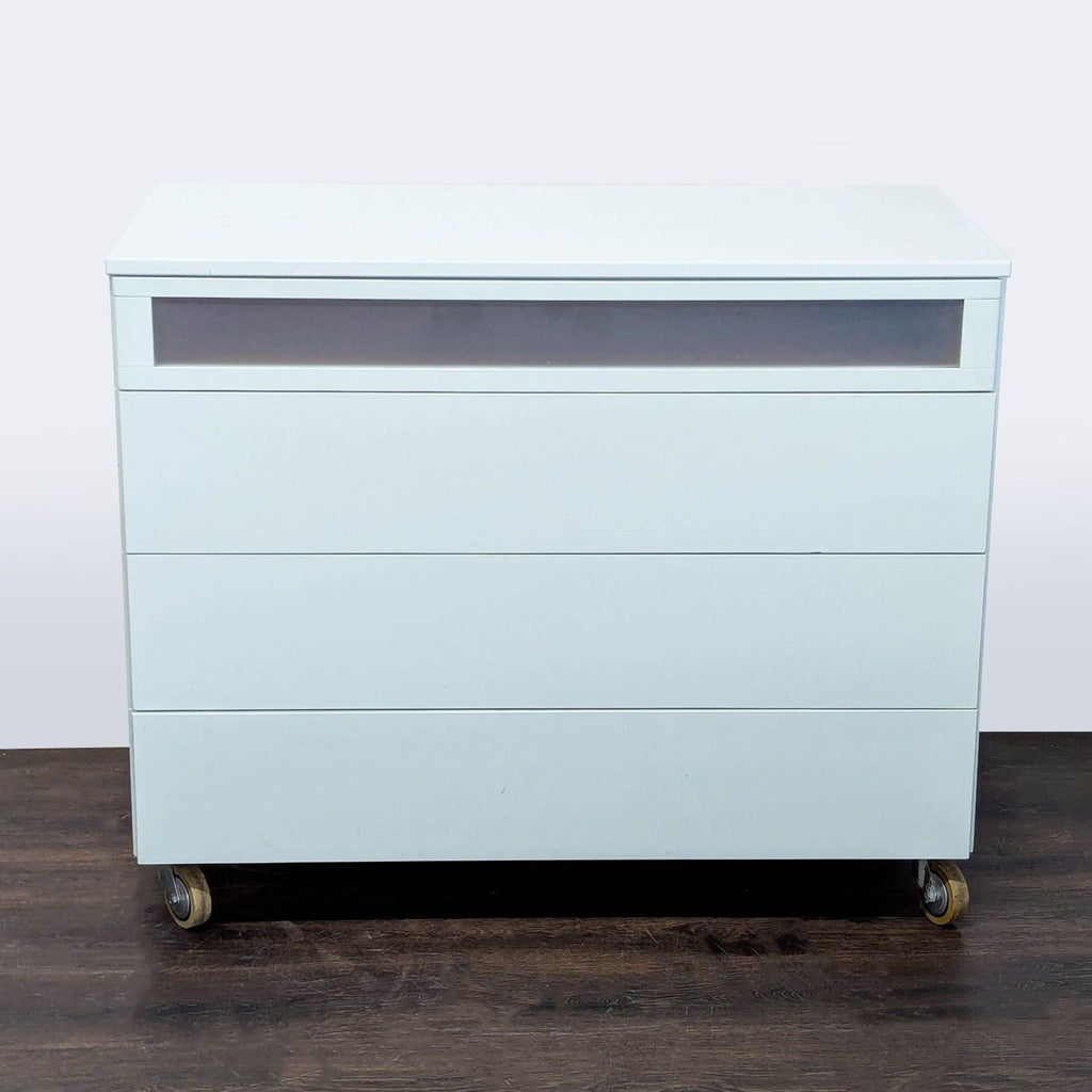 Modern white dresser with four drawers, including a frosted top drawer and wheels for easy mobility.