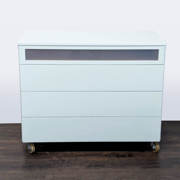 Modern white dresser with four drawers, including a frosted top drawer and wheels for easy mobility.