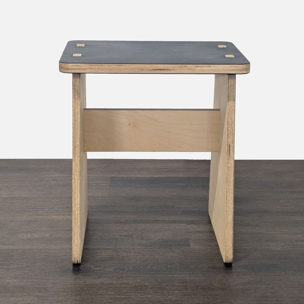 1. Minimalist side table with a black rectangular top and light wood base, shown from the front on a dark floor.  