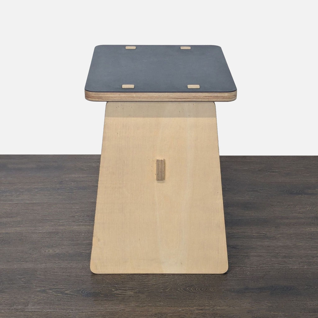 3. Side profile of a compact, light wood side table with a dark surface and square joints, on a dark floor.