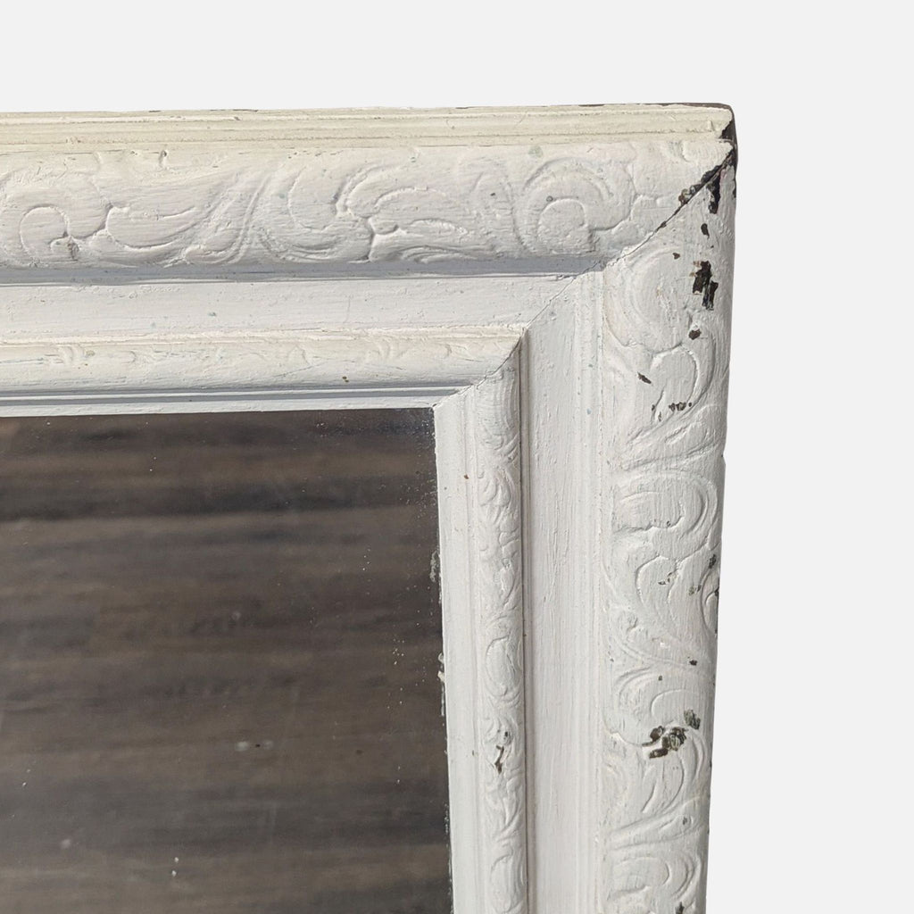 Close-up of a white, ornately carved mirror frame corner with visible chipped and distressed paint.