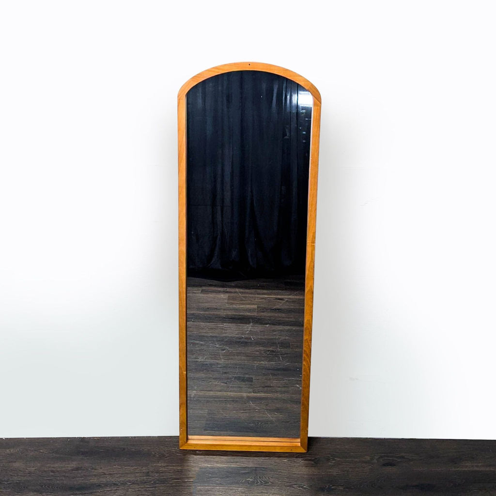 1. Full-length arched mirror with a wooden frame, shown standing upright against a white wall on a dark floor.