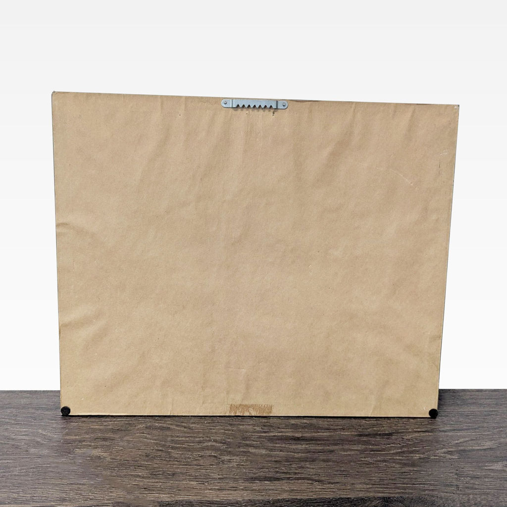 2. Back view of framed artwork, featuring brown paper backing and a metal hanging bracket at the top.  