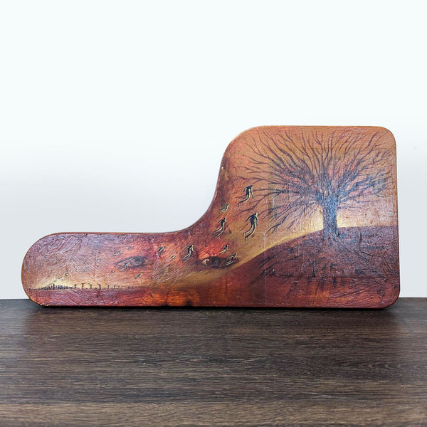 1. Artwork on shaped wood shows a dark tree, floating figures, and hidden eyes on a sunset landscape.