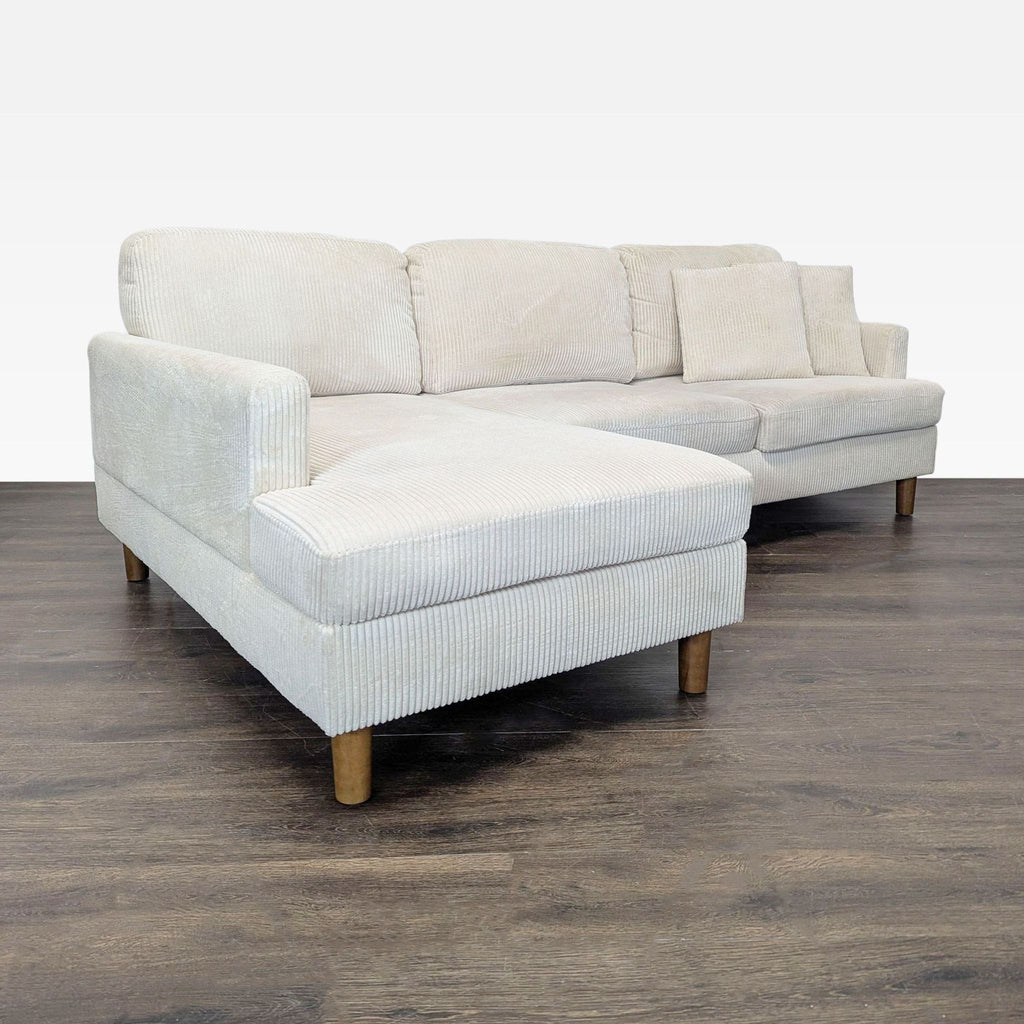 Angled view of a soft light beige corduroy sectional with chaise and wooden legs in a spacious setting.
