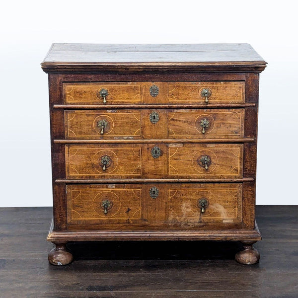 Antique wooden dresser with four drawers, ornate handles, wood inlay, and rounded feet, ideal for storage.