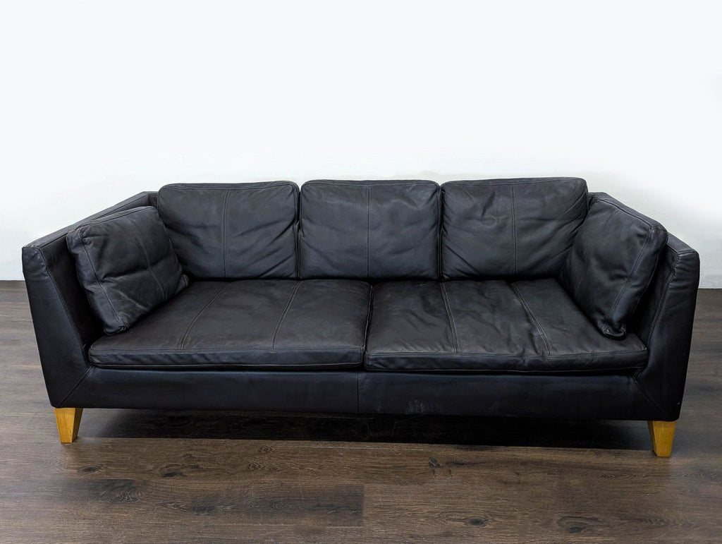 Sleek Ikea leather 3-seat sofa with wooden legs, offering modern and spacious comfort for living rooms.