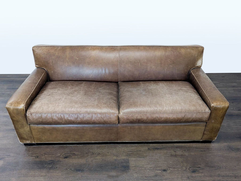 Vintage-look Mitchell Gold sofa for three, upholstered in brown leather with broad arms and natural wear.