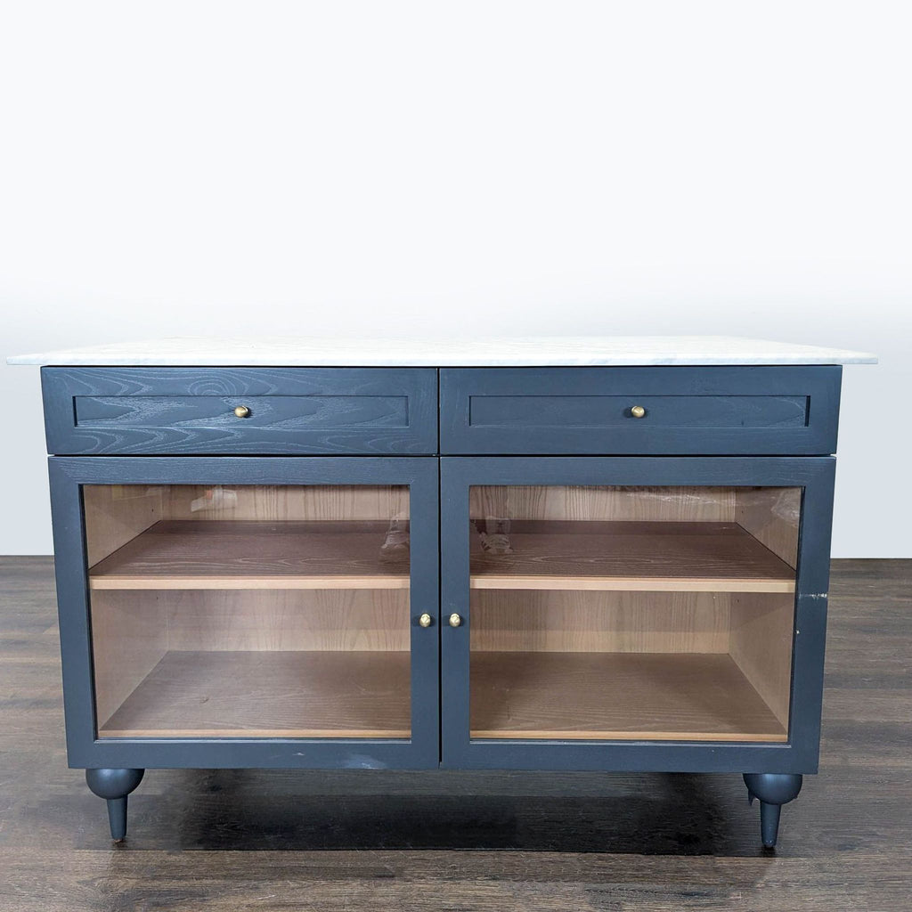 Dark blue Anthropologie kitchen island with marble top, two drawers, and double glass-door shelves.  