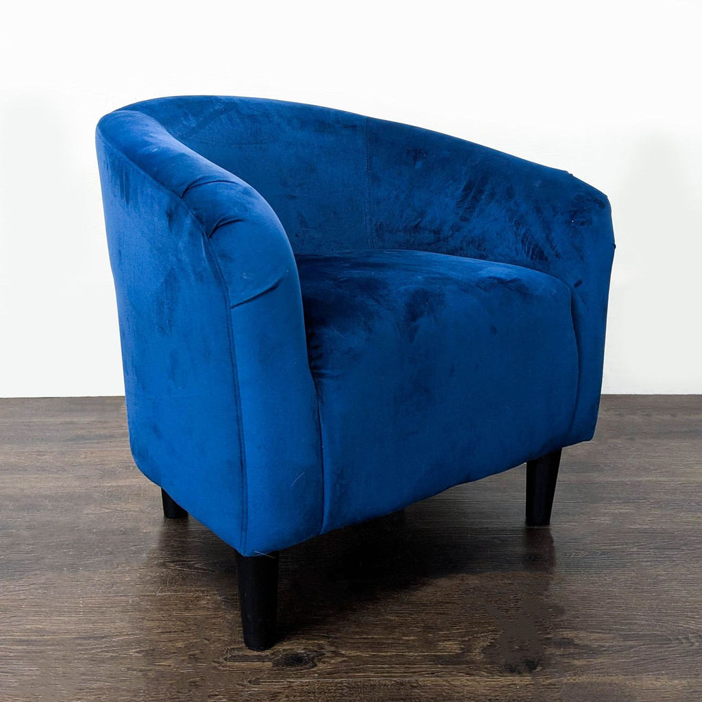 Blue velvet lounge chair featuring a curved back, plush upholstery, and sturdy black legs for support.