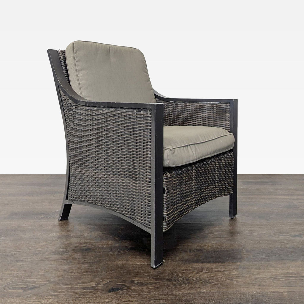 Side angle of a sturdy chair, showing woven wicker sides and thick, comfortable cushions on a dark frame.