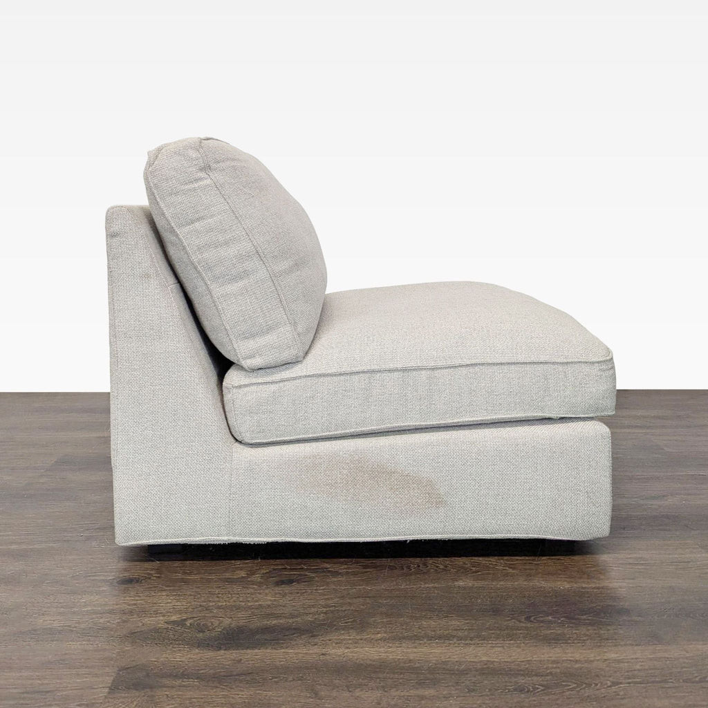 3. Side view of a simple, armless lounge chair featuring plush light cushions and a noticeable stain on one side.