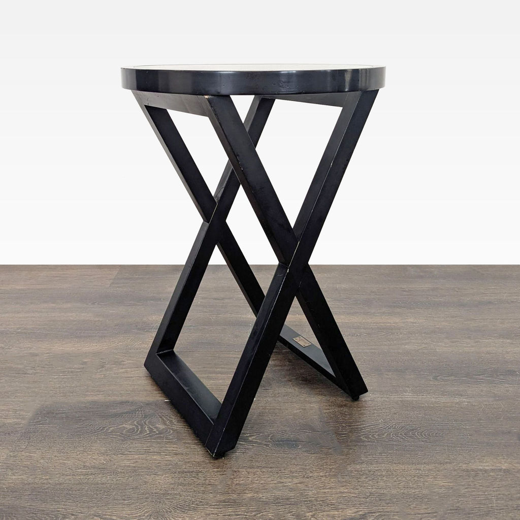 2. Contemporary round black end table featuring an X-shaped base on a wooden floor background.