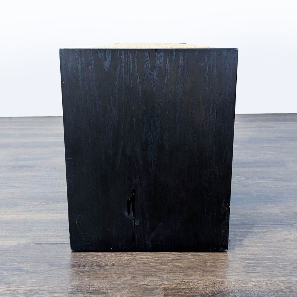 2. Side view of a black wooden West Elm bench with clean lines and minimalist design on wood flooring.