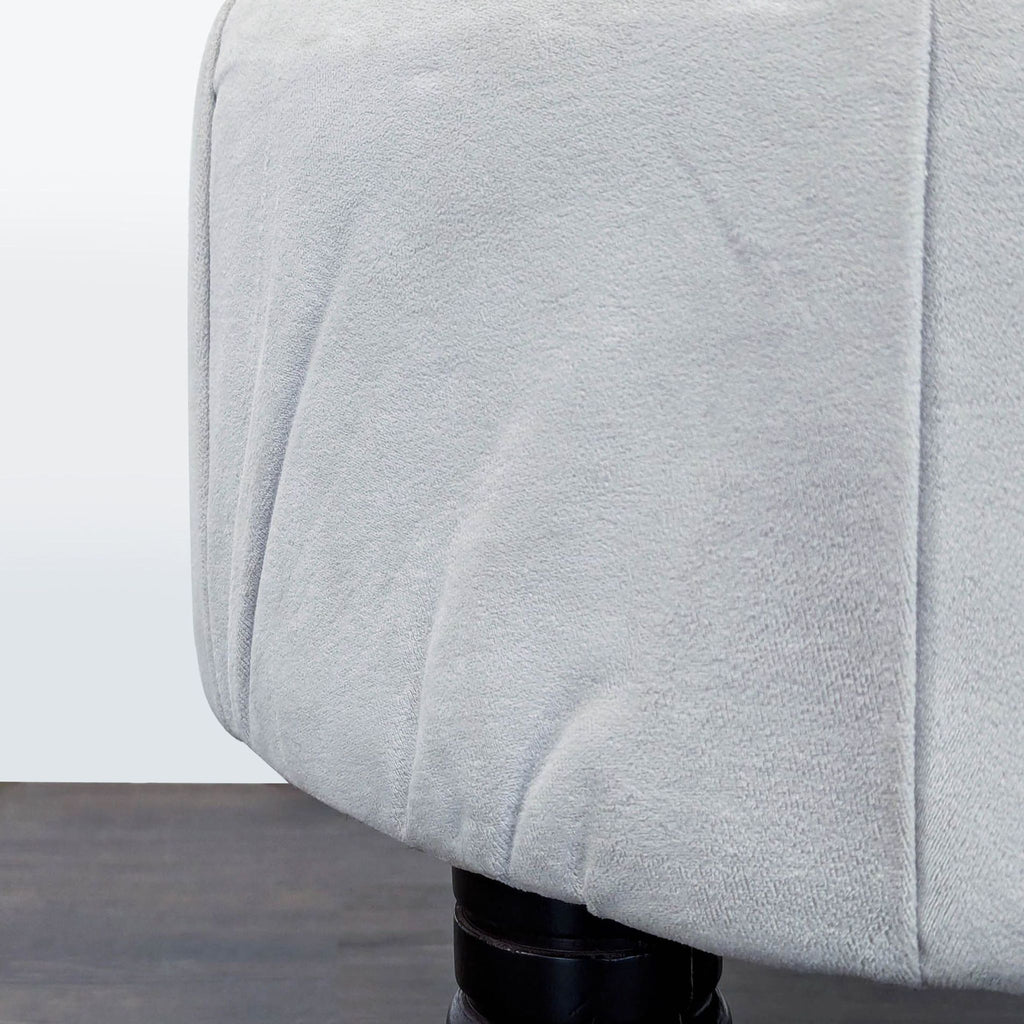 3. Close-up of the soft, light grey fabric and seam detail on the ottoman with part of a black wooden leg.