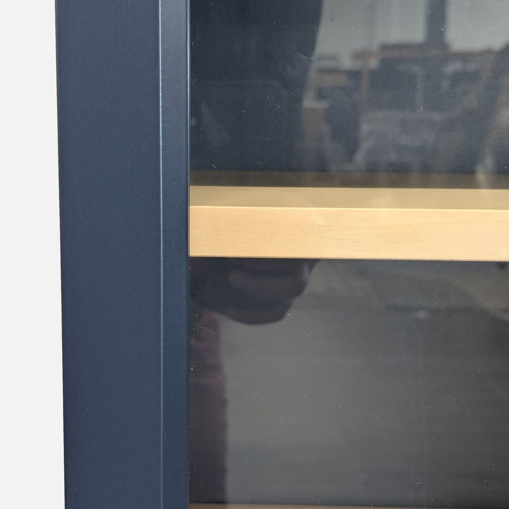 Sleek Ikea bookshelf in dark finish with glass doors, brass handles, and light wood shelves inside.