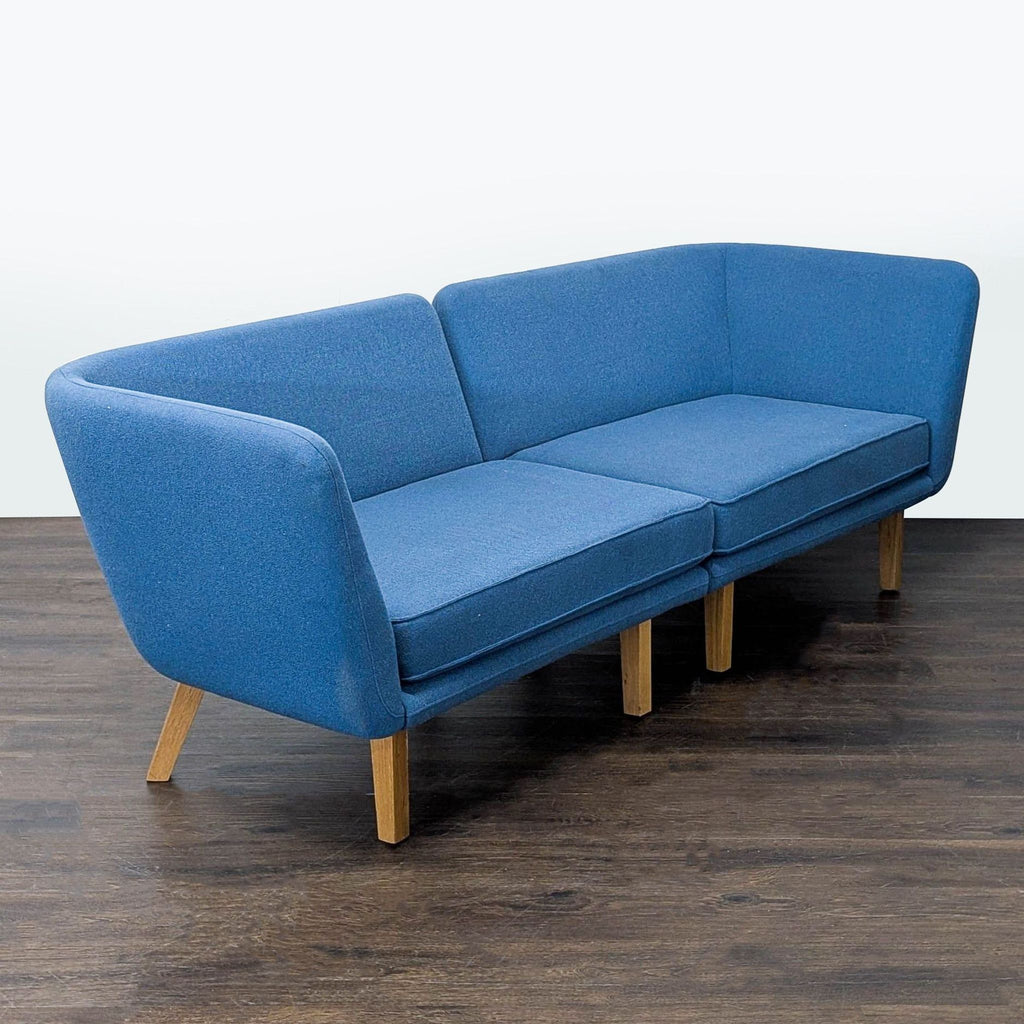 Angled view of a spacious Knoll sectional sofa with blue upholstery and sturdy wood base, offering comfort and style.  