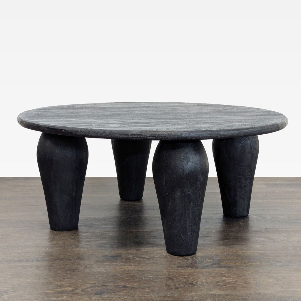 Four Hands coffee table with sturdy legs and a slim, round reclaimed wood top in light black finish.