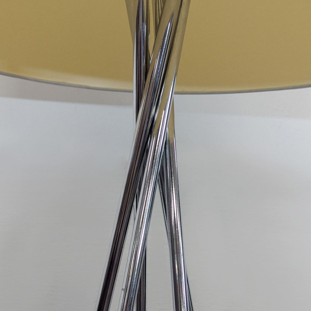 3. Close-up of intertwined chrome tripod legs beneath a white cylindrical lamp shade, category: Lighting.