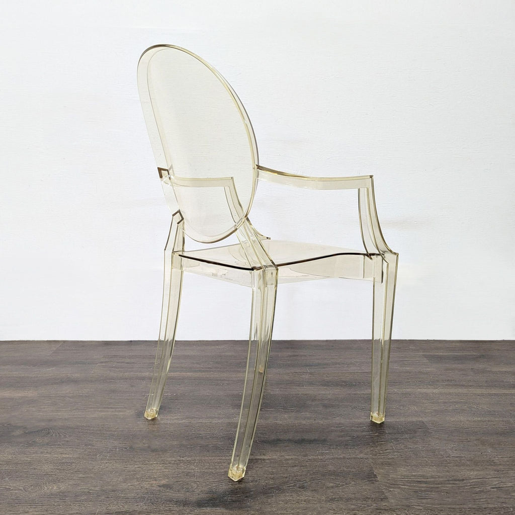 2. Side angle view of a clear acrylic dining chair with a curved oval back and modern armrests.