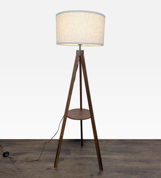 Modern tripod floor lamp with a wooden base, built-in shelf, and fabric shade for soft lighting.