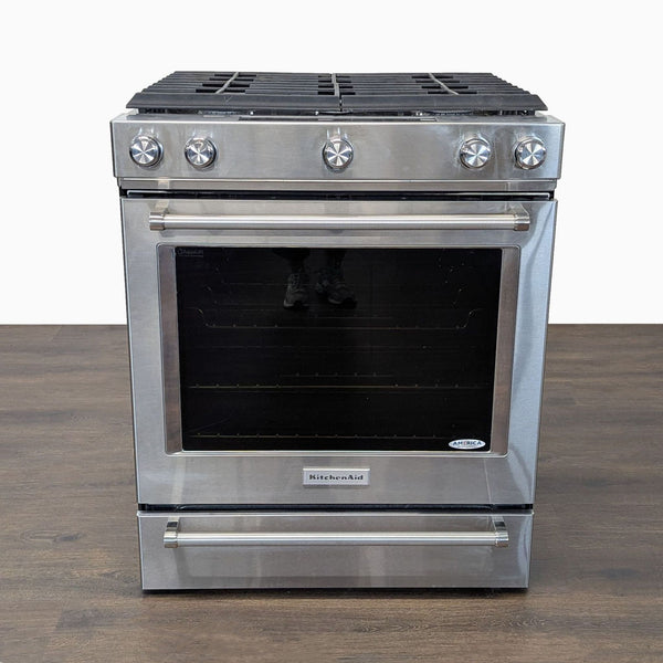 Sleek stainless steel KitchenAid stove and oven with five burner knobs and a large oven window.  