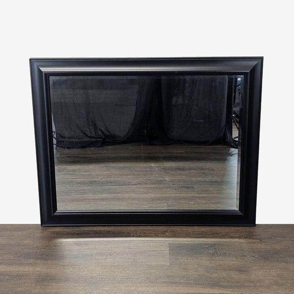 1. Rectangular mirror with a black frame, reflecting a wooden floor and dark curtain, placed against a wall.