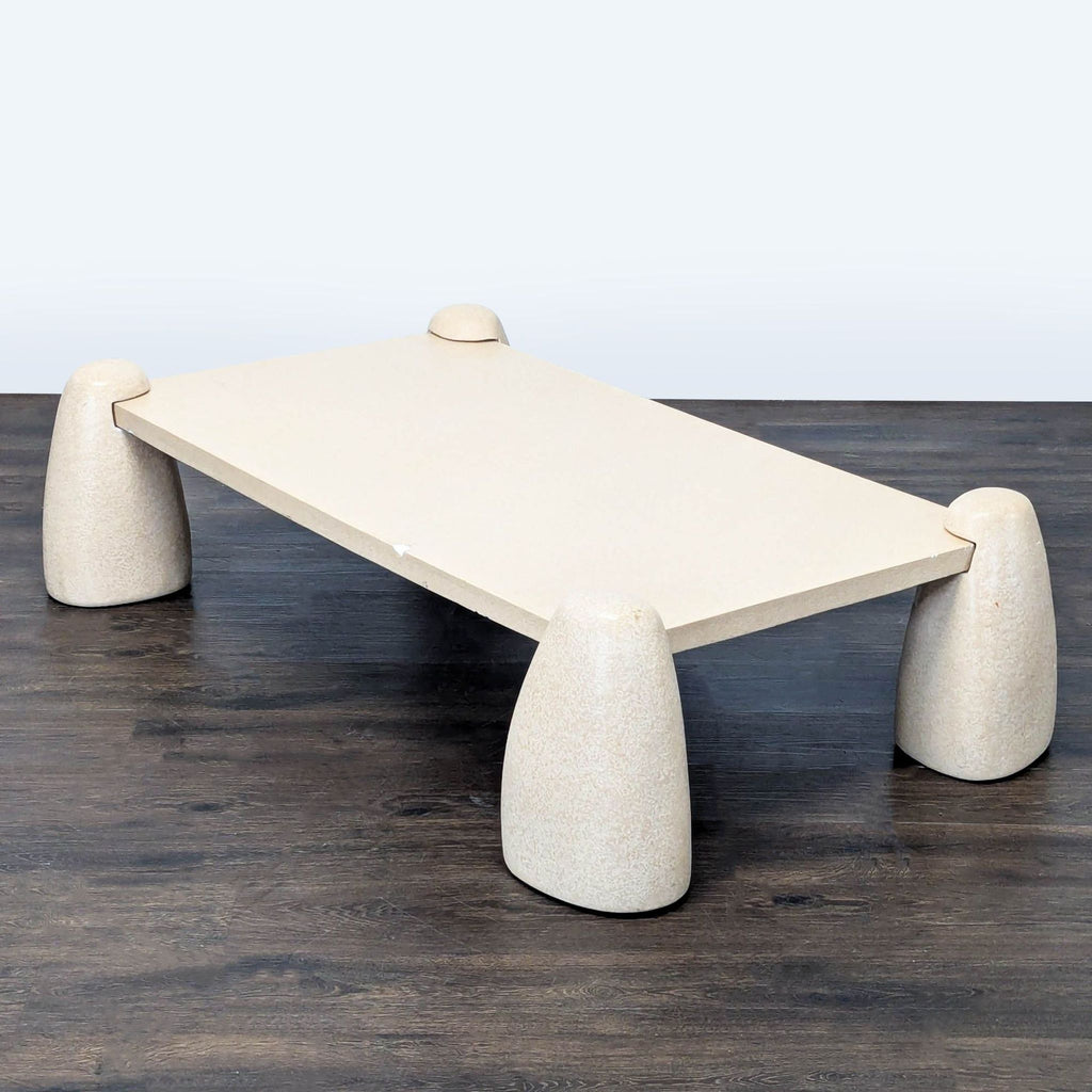 Modern coffee table by Sarah Sherman Samuel features textured concrete legs and a sleek sand-colored tabletop.