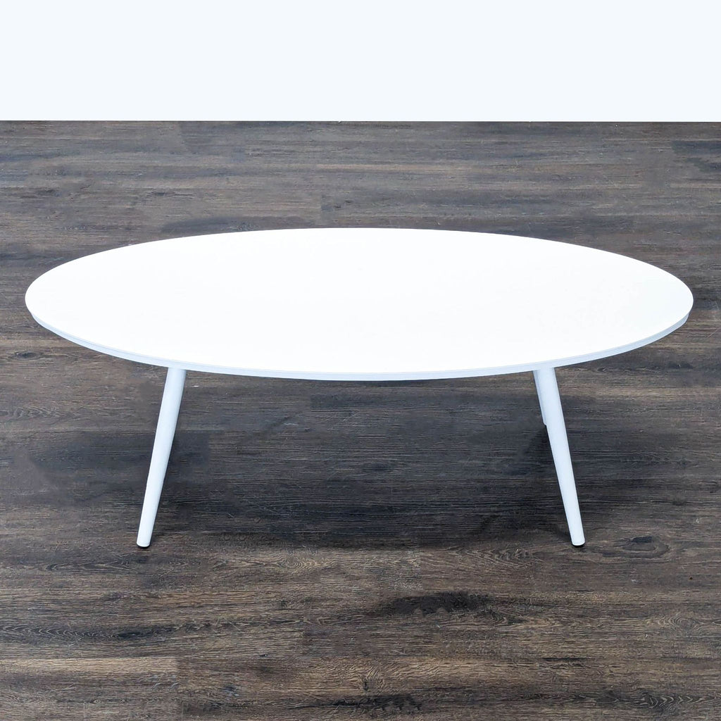 Modern Article coffee table featuring a white oval top and sturdy, angled wooden legs for versatile use.