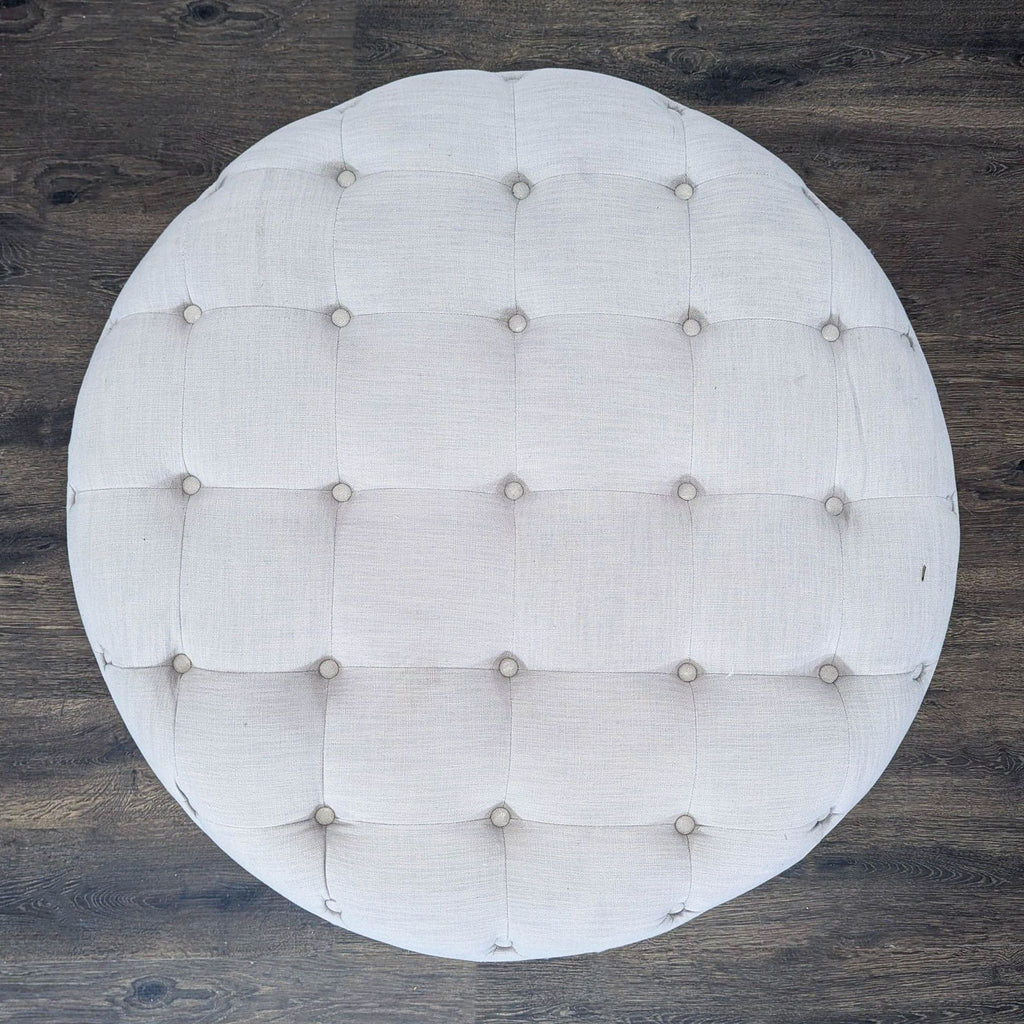 3. Top-down view of a large circular ottoman with a diamond-tufted gray fabric surface.