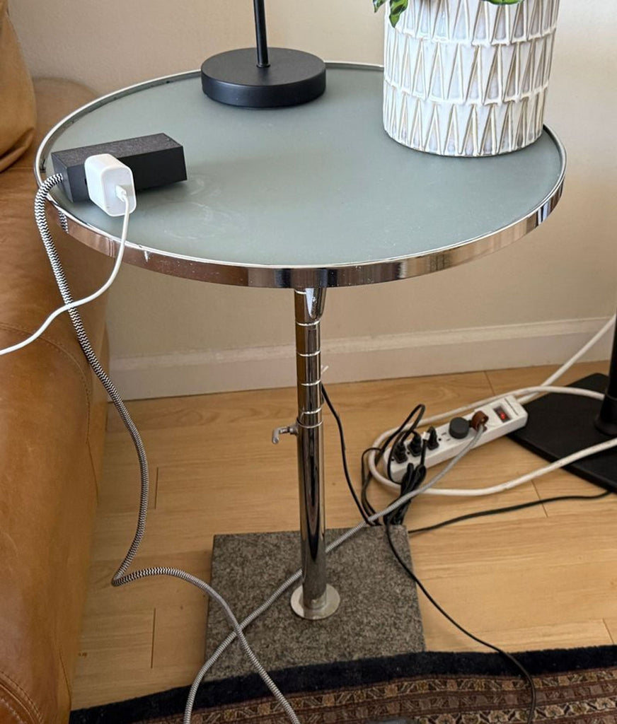 3. Contemporary side table with chrome finish features a lamp, planter, and device chargers in a living room setup.