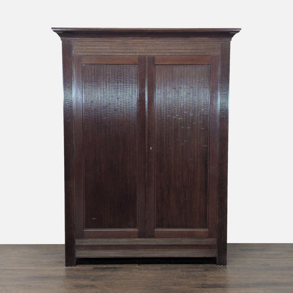 A dark wood Kerry Joyce armoire with elegant textured double doors, featuring a hanging rod and lower shelf.