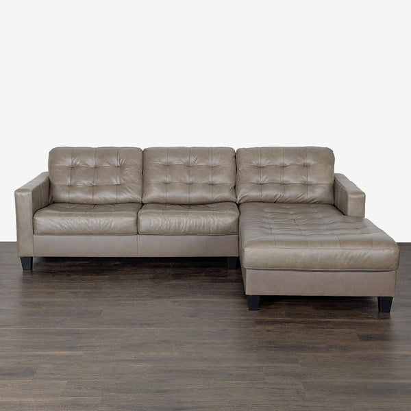 Taupe faux leather Ashley Furniture sectional with tufted details and spacious chaise, perfect for modern living rooms.