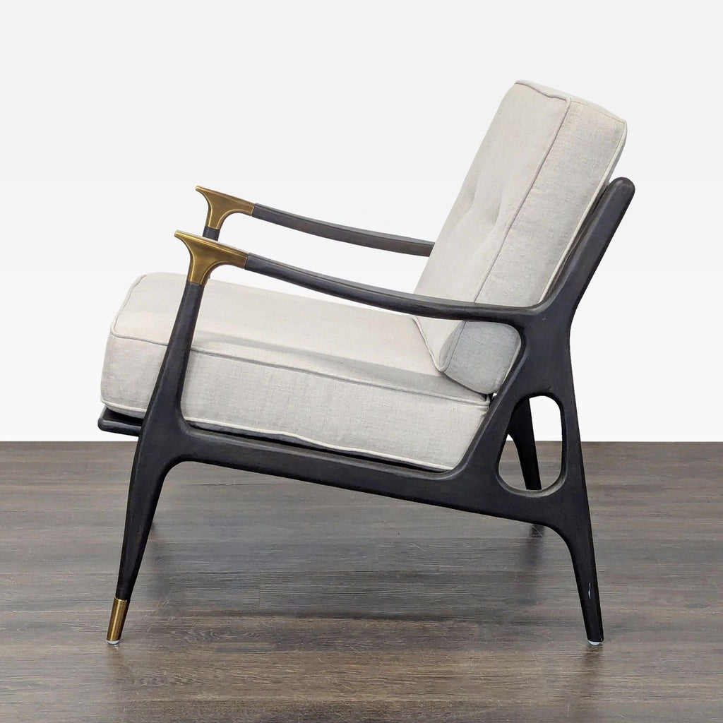 Stylish cream-cushioned lounge chair from Anthropologie with black wood and brass-accented arms and legs.