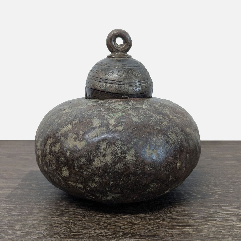 Sculptural cast bronze bell with aged patina, ornate collar engraving, and a suspended clapper visible inside.