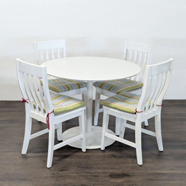 CB2 dining set with a white round table and four white chairs featuring striped cushions, ideal for modern spaces.  