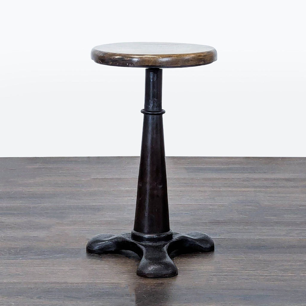 A metal stool with a round seat featuring a screw mechanism for height adjustment.  