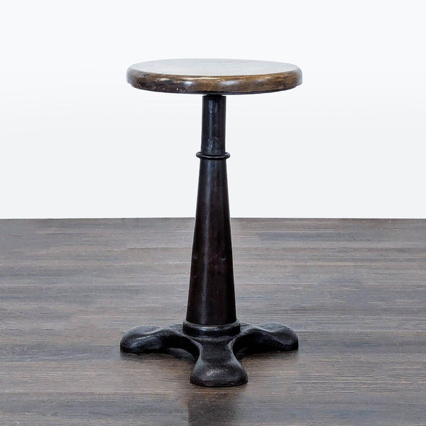 A metal stool with a round seat featuring a screw mechanism for height adjustment.  