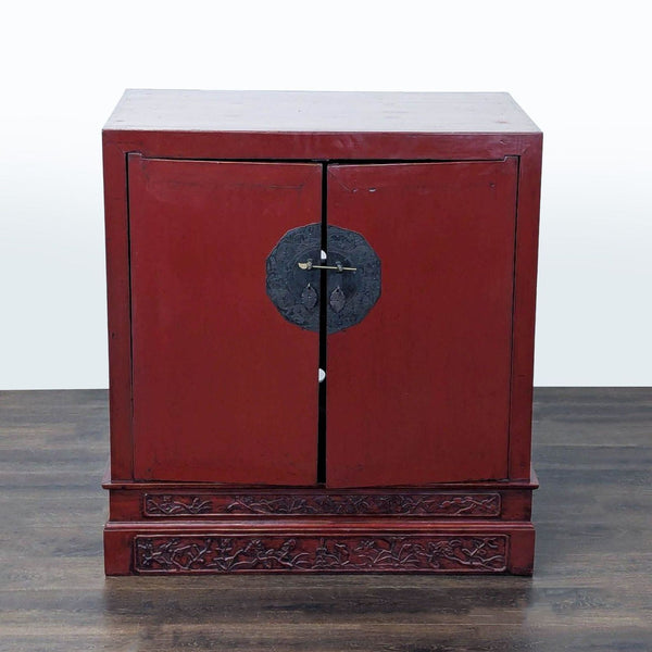 Red lacquer cabinet with carved base and engraved lock plate, showcasing intricate craftsmanship.  