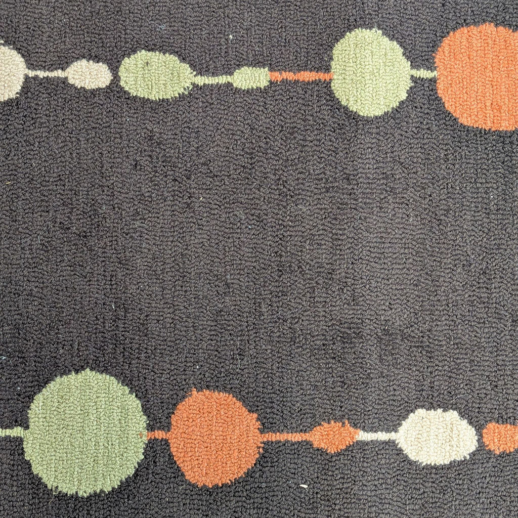 3. Detailed view of a rug’s colorful circle pattern in orange, green, and cream against a brown textured surface.