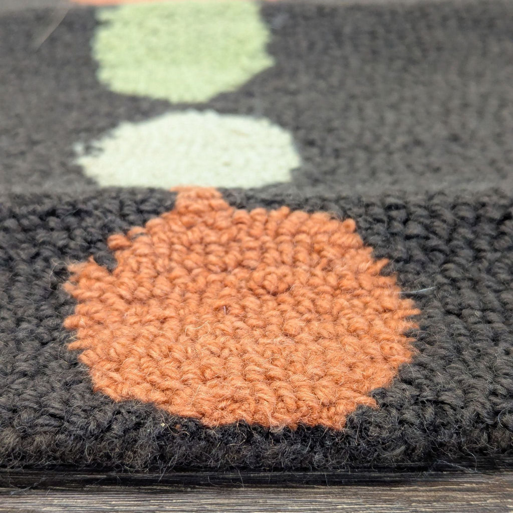 2. Close-up of textured looped yarn on a rug, showing orange, green, and cream circles on a dark background.