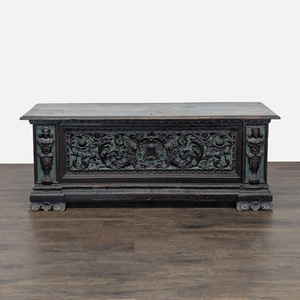 Intricate carvings with figurative details at corners and original metal hardware on a decorative object.
